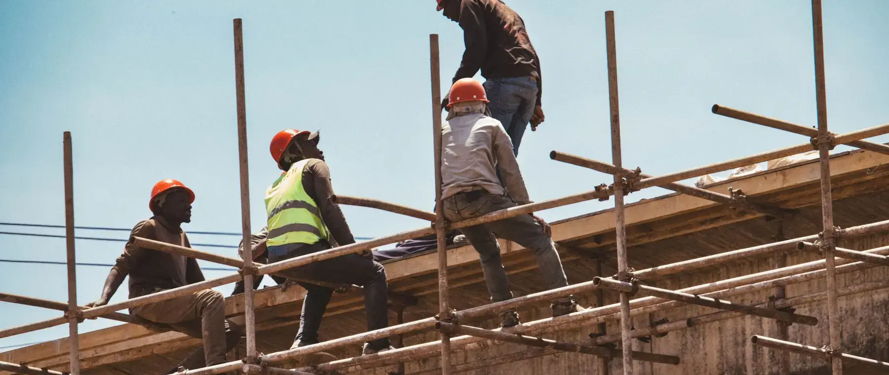 Construction workers on scaffolding erecting formwork against a clear sky