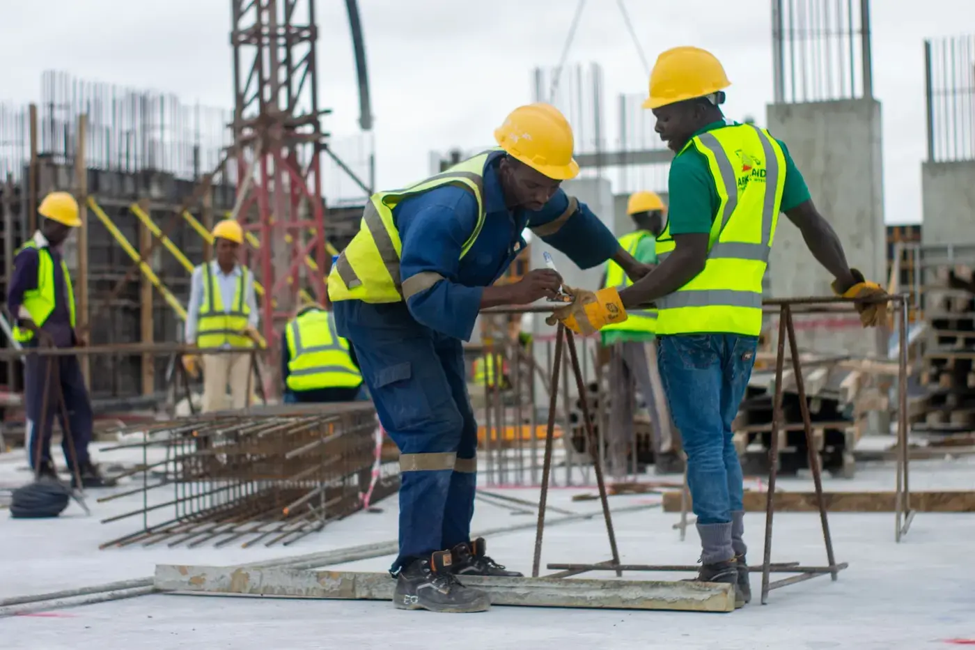 Two construction workers in high visibility vests and helmets tying reinforcement on site